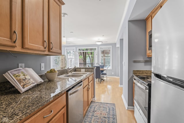 kitchen with brown cabinets, a sink, dark stone countertops, light wood finished floors, and stainless steel appliances