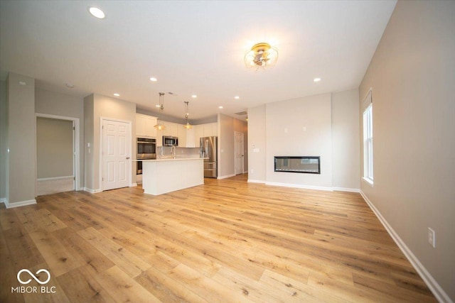9455 Orchard Cove Dr, Indianapolis, IN 46239 - unfurnished living room with a sink, a glass covered fireplace, recessed lighting, baseboards, and light wood-type flooring