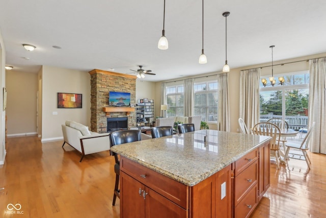 1361 Trescott Dr, Westfield, IN 46074 - kitchen featuring light wood-style floors, ceiling fan, a stone fireplace, decorative light fixtures, and baseboards