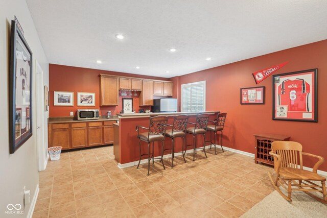 1361 Trescott Dr, Westfield, IN 46074 - kitchen with refrigerator, stainless steel microwave, a kitchen bar, baseboards, and brown cabinetry