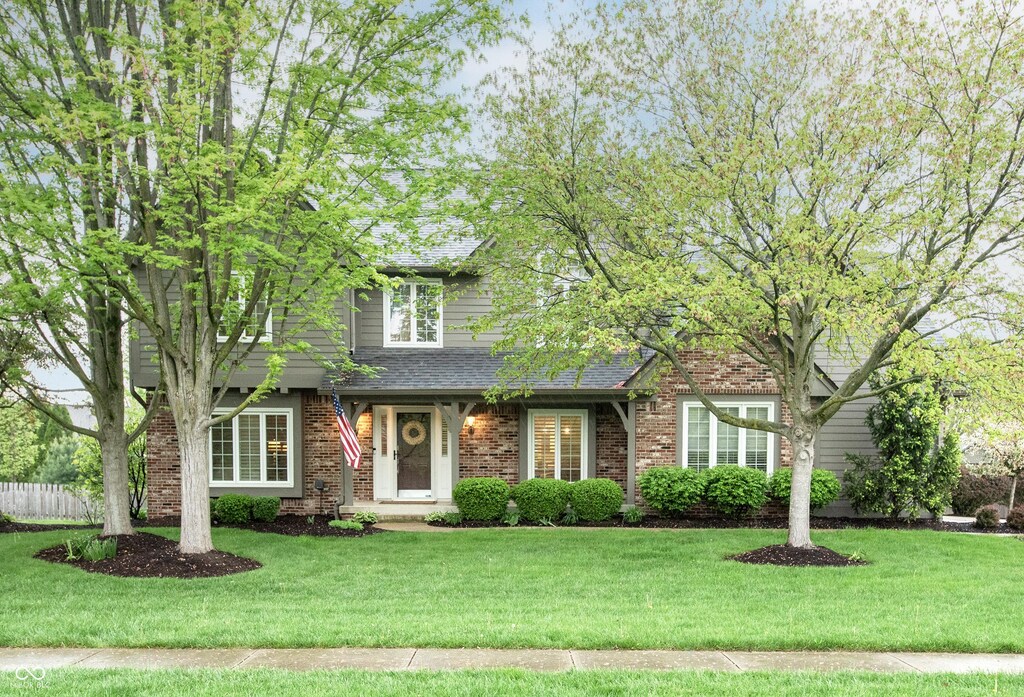 view of front of property with roof with shingles, a front lawn, and brick siding