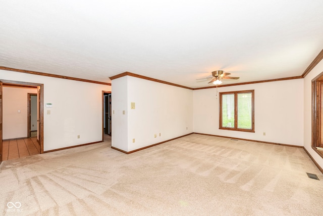 empty room with crown molding, a ceiling fan, visible vents, baseboards, and light colored carpet