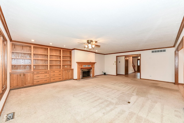 unfurnished living room featuring light colored carpet, visible vents, a ceiling fan, a fireplace with flush hearth, and crown molding