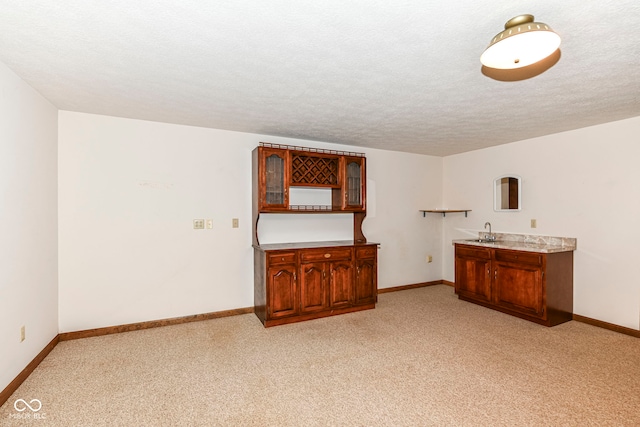 interior space with indoor wet bar, a textured ceiling, light carpet, and baseboards