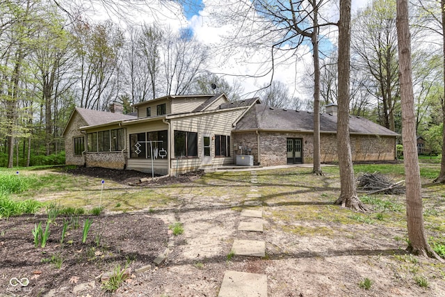 rear view of house with a sunroom, brick siding, and a chimney