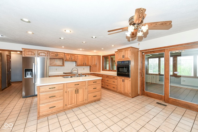 kitchen with black oven, a sink, light countertops, recessed lighting, and stainless steel refrigerator with ice dispenser