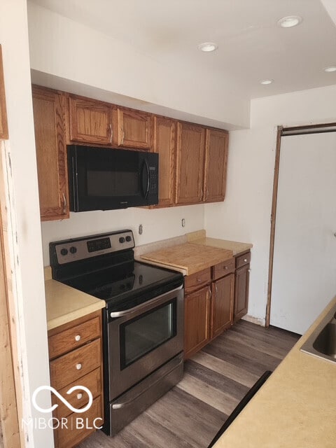 kitchen with black microwave, dark wood-type flooring, brown cabinets, and stainless steel range with electric stovetop