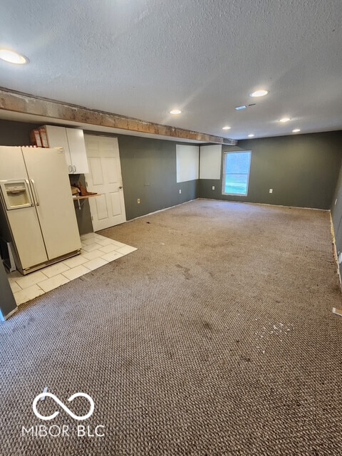 basement with light colored carpet, a textured ceiling, white fridge with ice dispenser, and recessed lighting