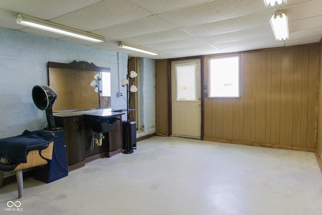 basement featuring a paneled ceiling and wood walls