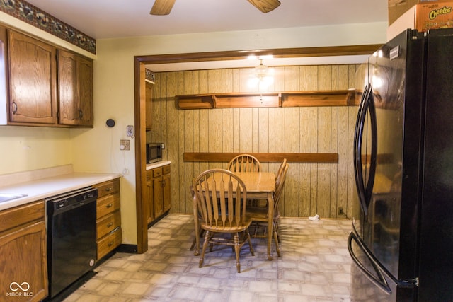 kitchen with black appliances, wooden walls, light floors, light countertops, and a ceiling fan
