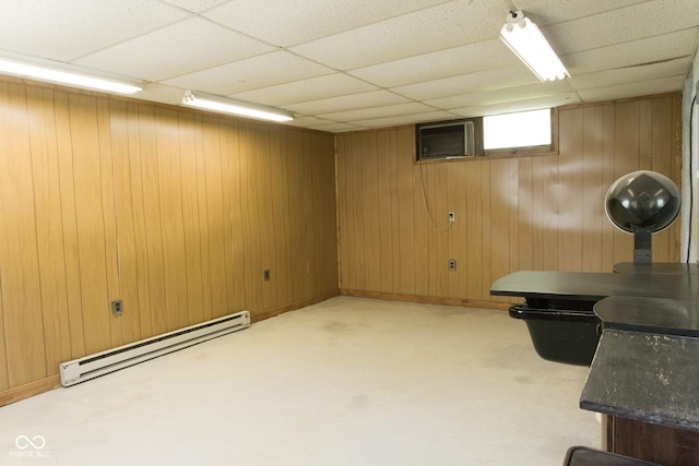 basement with a baseboard radiator, a paneled ceiling, wooden walls, and light colored carpet
