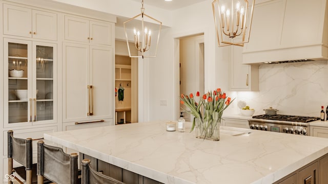 8082 Abington Way, Zionsville, IN 46077 - kitchen featuring light stone counters, tasteful backsplash, a chandelier, glass insert cabinets, and custom range hood