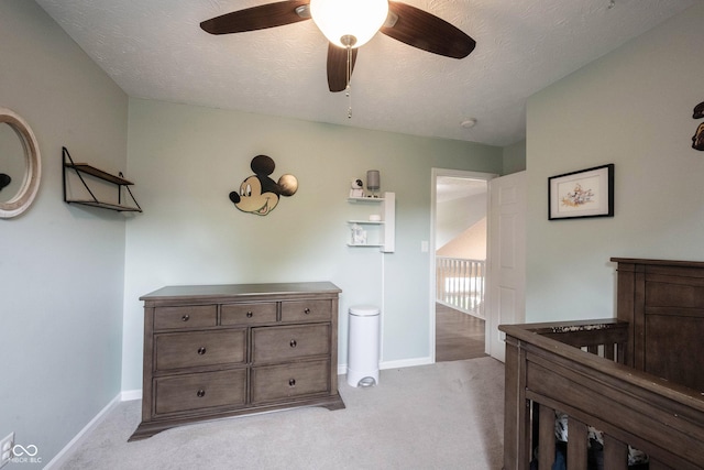 bedroom featuring light colored carpet, baseboards, ceiling fan, a textured ceiling, and a crib