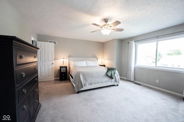 bedroom with light colored carpet, a textured ceiling, baseboards, and a ceiling fan