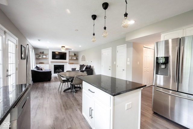 kitchen featuring stainless steel appliances, light wood-style floors, a fireplace, white cabinetry, and dark stone counters