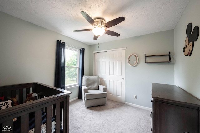 bedroom featuring light colored carpet, a textured ceiling, baseboards, a crib, and a closet