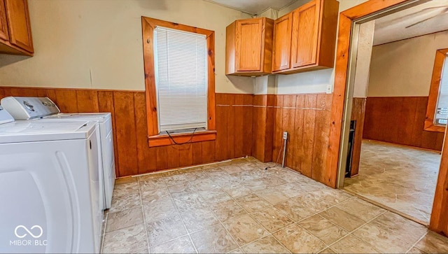 laundry room featuring wooden walls, washer and dryer, cabinet space, a wainscoted wall, and stone finish flooring
