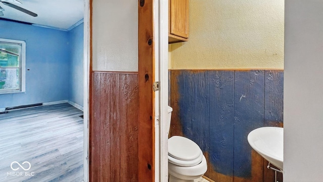 bathroom featuring wood finished floors, toilet, wood walls, and wainscoting