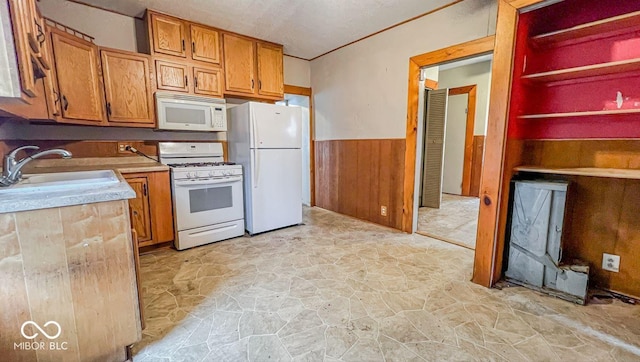 kitchen featuring a sink, wainscoting, white appliances, brown cabinets, and stone floors