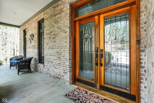 doorway to property featuring covered porch and brick siding