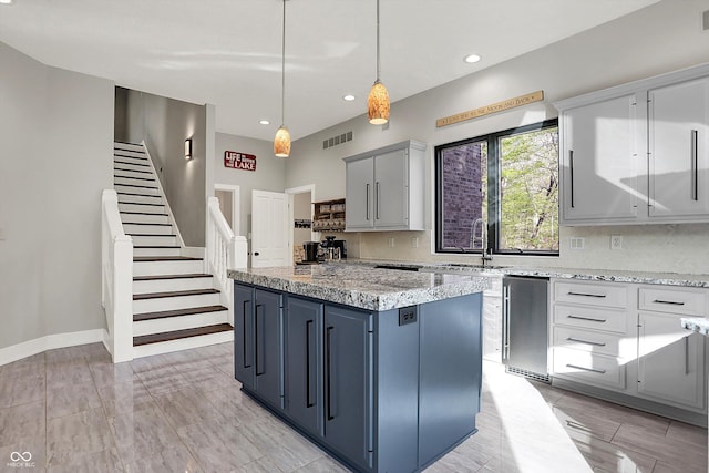 kitchen with visible vents, a kitchen island, tasteful backsplash, light stone counters, and a sink