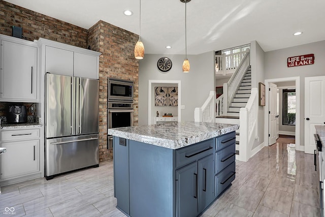 kitchen featuring appliances with stainless steel finishes, hanging light fixtures, light stone counters, and white cabinets