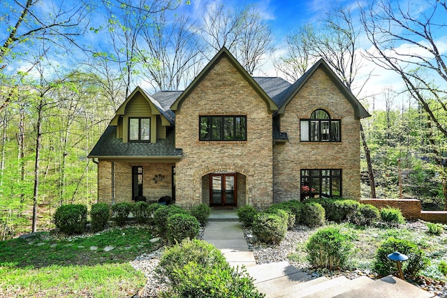 tudor-style house featuring french doors, roof with shingles, and brick siding