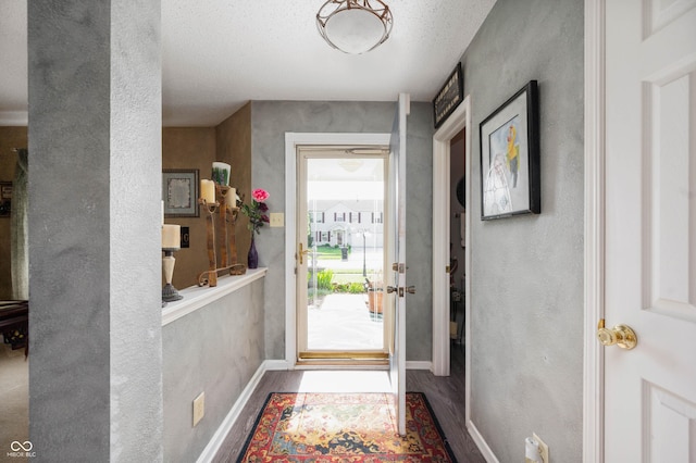doorway to outside featuring a textured ceiling, a textured wall, baseboards, and wood finished floors