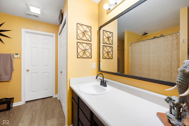bathroom with vanity, a textured ceiling, baseboards, wood finished floors, and visible vents