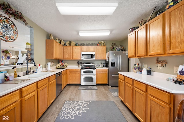kitchen with a sink, light countertops, a textured ceiling, light wood-style flooring, and stainless steel appliances