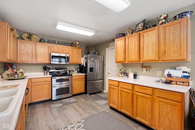 kitchen with light countertops, stainless steel appliances, light wood-type flooring, and a textured ceiling