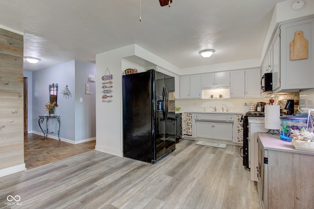 kitchen featuring light wood finished floors, a sink, baseboards, light countertops, and black appliances
