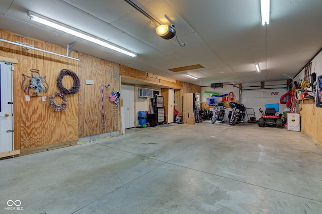garage featuring a garage door opener, wood walls, and a wall unit AC