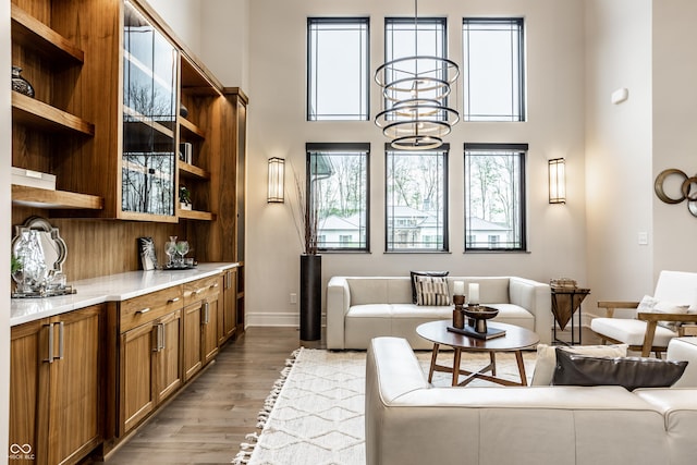 living area featuring baseboards, a towering ceiling, wood finished floors, and an inviting chandelier