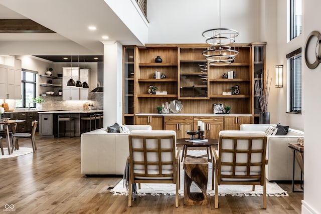 bar featuring wall chimney range hood, tasteful backsplash, light wood-type flooring, a towering ceiling, and pendant lighting