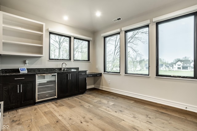 kitchen with wine cooler, dark cabinetry, light wood-style flooring, and visible vents