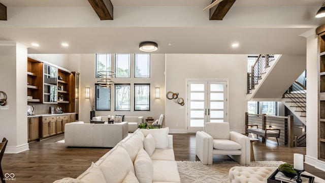 living room with french doors, a towering ceiling, dark wood finished floors, beam ceiling, and stairway