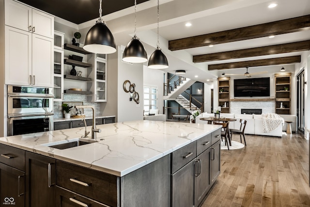 kitchen with open shelves, stainless steel double oven, a sink, a fireplace, and light wood-style flooring