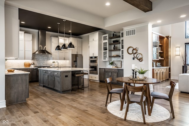 kitchen featuring wall chimney range hood, open shelves, appliances with stainless steel finishes, tasteful backsplash, and visible vents
