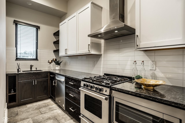 kitchen featuring open shelves, wall chimney exhaust hood, a sink, dark stone countertops, and appliances with stainless steel finishes
