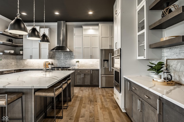 kitchen with open shelves, wall chimney exhaust hood, stainless steel appliances, decorative backsplash, and light wood-type flooring