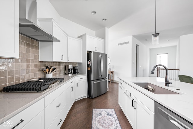 kitchen with wall chimney range hood, a sink, stainless steel appliances, backsplash, and visible vents