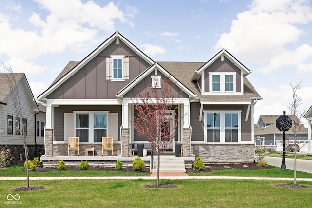craftsman inspired home with covered porch, board and batten siding, a front yard, and stone siding