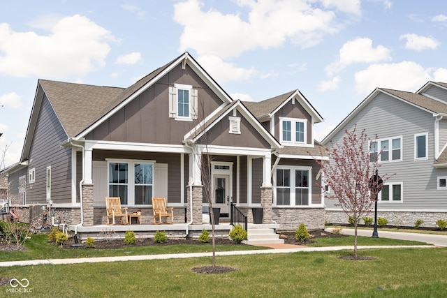 craftsman-style home with covered porch, board and batten siding, a front lawn, and stone siding