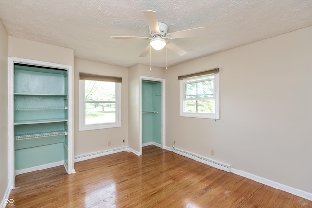 unfurnished bedroom featuring two closets, baseboards, a textured ceiling, baseboard heating, and wood finished floors