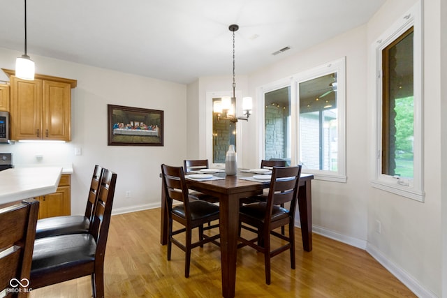 dining area with visible vents, light wood-style flooring, baseboards, and an inviting chandelier