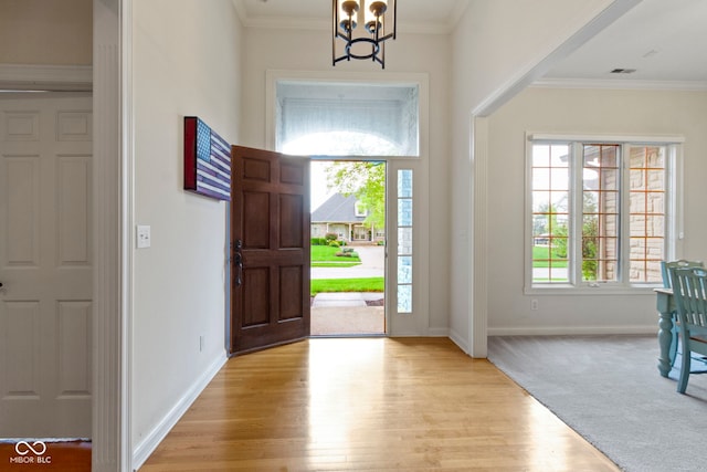foyer featuring crown molding, an inviting chandelier, light wood finished floors, baseboards, and visible vents