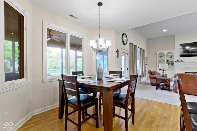 dining room featuring visible vents, a fireplace, baseboards, light wood finished floors, and ceiling fan with notable chandelier