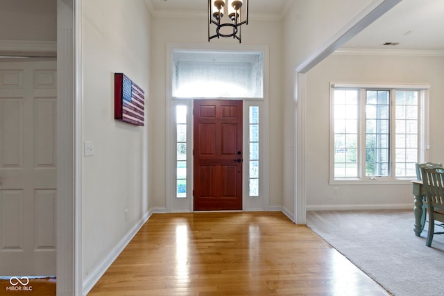 entrance foyer featuring light wood-style floors, a chandelier, baseboards, visible vents, and ornamental molding