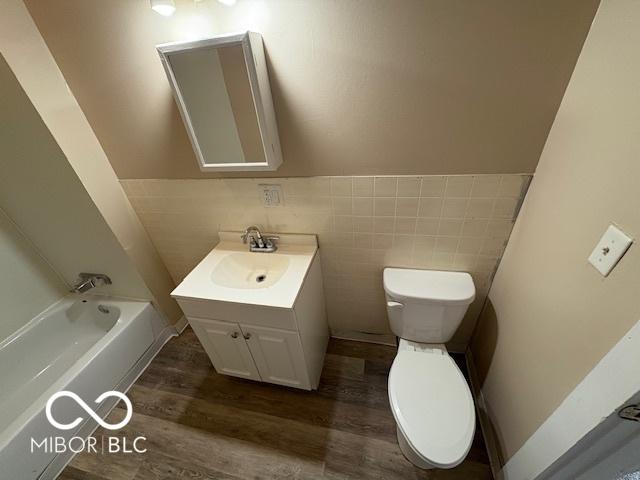 2413 N Macedonia Ave, Muncie, IN 47303 - full bathroom featuring vanity, wood finished floors, a tub to relax in, wainscoting, and tile walls